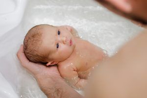 First bath. Newborn baby bathing held by father and looking at him very seriously. Baby care.